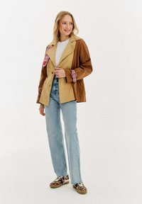 Hnedo-bežová prešívaná bunda s kockovanými akcentmi, kombinovaná s svetlomodrými džínsami a teniskami s leopardím potlačou. Štruktúrovaná tkanina a kontrastné farby.