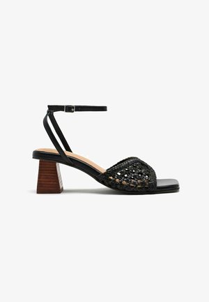 Sandale noire à talons avec dessus tissé, bout ouvert et bride de cheville. Talon bloc avec une texture bois. Semelle intérieure noire lisse.