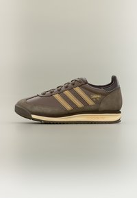 Brūnas ādas sporta kurpes ar zamšādas akcentiem, trim zelta svītrām un fakturētu zoli. Uz kurpes sāniem ir izšūts dizains un retro zīmola apdruka.