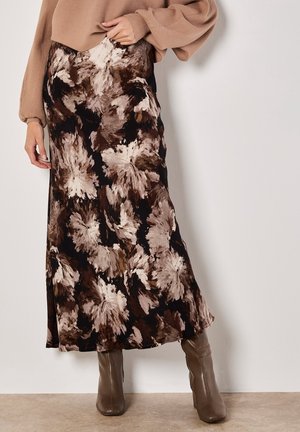 Kvinde iført en brun og beige abstrakt blomster midi-nederdel, tan sweater med ballonærmer og taupe ankelstøvler med hæl.