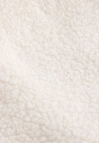 Pehmeä, teksturoitu kangas hieman valkoisena, jossa on pörröinen, pehmeä pinta, jossa on pieniä käärittyjä kuituja, sopii vaatteisiin tai kodintekstiileihin.