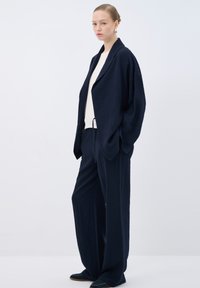 Navy blue textured outfit featuring a loose-fitting jacket and wide-leg pants, paired with a cream top and black slip-on shoes.