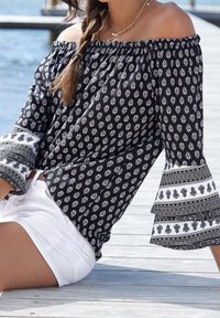 Blouse marine à épaules nues avec des motifs floraux blancs ; possède des manches volantes avec un ourlet contrasté. Associée à un short blanc.