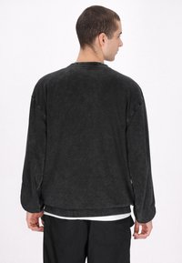 Schwarzes Langarmshirt mit lockerer Passform, geripptem Halsauschnitt und weichem, strukturiertem Stoff. Verfügt über einen geraden Saum und überschnittene Schultern.
