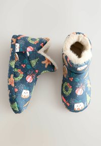 Cozy blue slippers with plush white fur lining, featuring colorful holiday-themed prints including gingerbread men, ornaments, and trees.