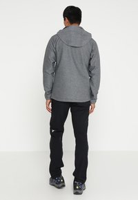 Sweatshirt à capuche gris avec manches longues, en tissu texturé et coupe décontractée, associé à un pantalon de plein air noir et des chaussures noires robustes.