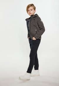 Grå zip-up jacka med huva, som har två framfickor, bärs över en svart skjorta och svarta skinny jeans. Avslutas med vita sneakers.