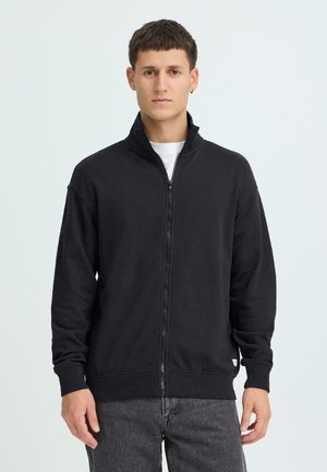 Zwarte sweatvest met ritssluiting, gemaakt van zachte stof, met een hoge kraag, geribbelde zoom en manchetten, en een klein logo aan de onderkant links.