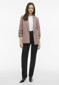 Světle růžový saka se zapínáním na jeden knoflík, kombinovaný s bílým tričkem a černými kalhotami s vysokým pasem. Slim-fit silueta.