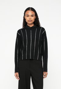 Czarny sweter wykonany na drutach z pionowymi srebrnymi paskami, wysoki ko�łnierz i długie rękawy. Ma fakturę ribbed i skrócony krój.