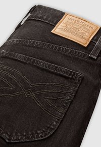 Zwarte denim jeans gevouwen, met de achterzak zichtbaar waarin stikdetails en een tan Levi Strauss & Co. leren merkpatch boven de tailleband zijn te zien.