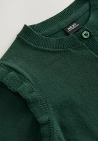 Grüne Strickjacke aus weichem Strickstoff, mit Rundhalsausschnitt, Knopfverschluss und Rüschendetails entlang der Schulternähte.