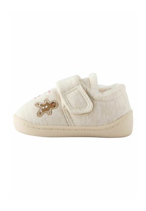 Chaussure beige douce pour tout-petit avec sangle en velcro et petite décoration bonhomme en pain d'épice sur le côté, semelle légèrement relevée au niveau des orteils et du talon.