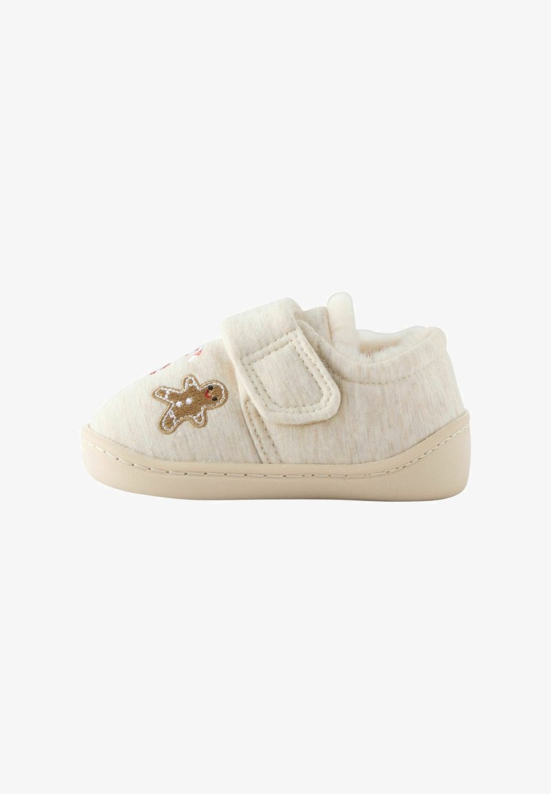 Chaussure beige douce pour tout-petit avec sangle en velcro et petite décoration bonhomme en pain d'épice sur le côté, semelle légèrement relevée au niveau des orteils et du talon.