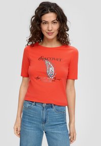 Czerwona bawełniana koszulka z krótkim rękawem, z czarnym napisem i grafiką na przodzie. Połączona z niebieskimi dżinsowymi spodniami o wysokim stanie.