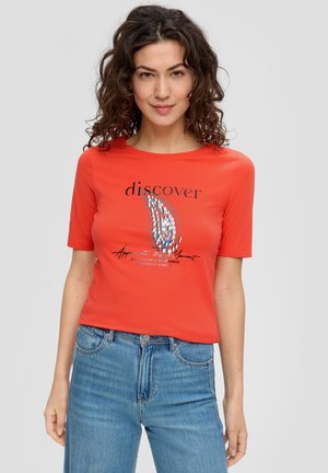 Red cotton t-shirt with short sleeves featuring black text and graphic design on the front. Paired with blue denim high-waisted jeans.