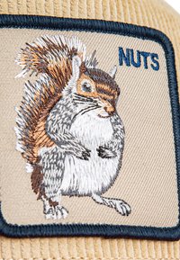 Bežani kordura zakrpa s izvezenim sivim vjevericom koja drži orahe, s plavim natpisom "NUTS" u kontrastnom fontu.