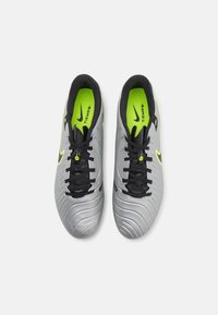 Football boots with a silver synthetic upper, black laces, black lining, and neon yellow accents; textured surface and sleek design.