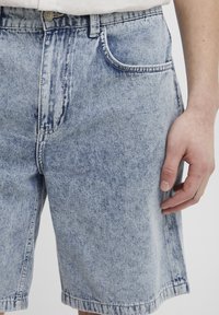 Light blue denim shorts with a faded finish, featuring a front pocket, belt loops, and a straight cut above the knee.