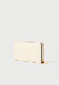 Crème-kleurige leren portemonnee met een gladde textuur, goudkleurige rits en een subtiele reliëflogo op de voorkant. Rechthoekige vorm, slank ontwerp.