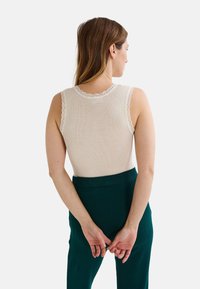 Débardeur en crème à bordure en dentelle et à côtes, présentant une silhouette ajustée. Associe à un pantalon taille haute vert foncé.
