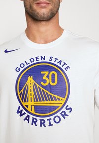 Hvid bomulds T-shirt med en rund grafik i blå og gule farver, der viser "GOLDEN STATE WARRIORS" og "30" med en broillustration.