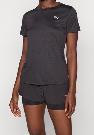 Kvinde iført en tætsiddende mørkegrå Puma t-shirt og sorte træningsshorts med delvist synligt indvendigt kompressionslag.