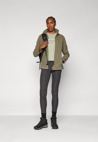 Green fleece jacket with zippered pockets, light gray t-shirt, dark gray leggings, and black hiking boots with laces and textured soles.