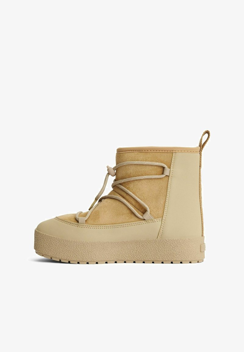 Beige ruskind og gummi ankelstøvle med en tekstureret sål, front snørelukning og en løkke ved hælen for nem påtagning.