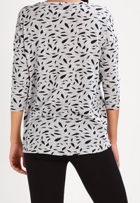 Haut gris avec un motif de feuilles noires, col rond et manches trois quarts, associé à des leggings noirs. Tissu doux et texturé.