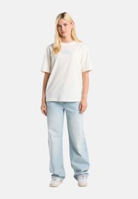 Cream cotton t-shirt with short sleeves and blue graphic text, paired with light blue wide-leg jeans and white sneakers.
