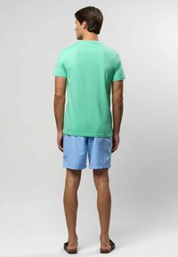 Müntzroheline lühikeste varrukatega T-särk, pehme puuvillane materjal, paaritatud helesiniste lühikeste pükste ning pruunide sandaalidega. Tagantvaade, lihtne disain.