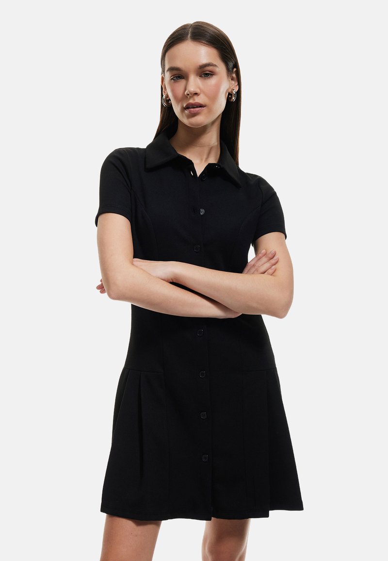 Schwarzes kurzärmeliges Kleid mit Kragen, Knopfleiste und plissiertem Rock. Aus einem glatten Stoff mit tailliertem Schnitt gefertigt.