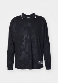 Svart långärmad Nike-polo med subtilt upprepande "Nike Air"-tryck och vitkantad krage, med en liten rektangulär logopatch nära fållen.