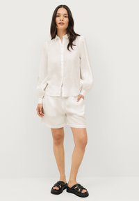 Witte linnen overhem samengestelde shirt met lange gepofte mouwen, gecombineerd met bijpassende shorts. Zwarte slide sandalen met dikke bandjes.