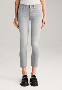 Világosszürke, slim fit farmernadrág, szakadt szegéllyel, klasszikus, öt zsebes dizájnnal és elöl gombos zárással, fényes fekete loaferekkel párosítva.