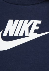Φούτερ Nike σε ναυτικό μπλε χρώμα με μεγάλο λευκό λογότυπο "NIKE" και σχέδιο σβούρες. Το ύφασμα είναι πλεκτό με ομαλή υφή. Απλός, τολμηρός σχεδιασμός.