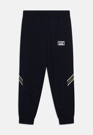 Czarne spodnie dresowe z elastycznym pasem, bocznymi kieszeniami, białymi ukośnymi paskami na nogawkach i białym logo EA7 Emporio Armani na prawej udzie.
