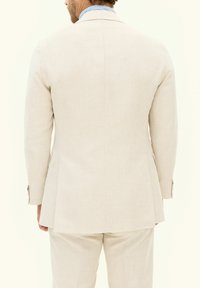 Ljus beige linnekostym med en strukturerad design. Har en notch-lapel, långa ärmar och subtil textur. Bakifrån syns den skräddarsydda passformen.