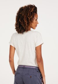 Svetlá polokošeľa s krátkymi rukávmi a vyrolovanými manžetami, textúrovaným detailom na zadnej strane, spárovaná s tmavými, ušitými nohavicami s pruhovaným pásom.