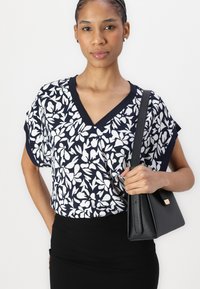 Navy V-Ausschnitt Bluse mit weißem Blumenmuster, kurzen Ärmeln, kombiniert mit einer schwarzen strukturierten Handtasche, die am Schulter getragen wird. Schwarzer Bleistiftrock.