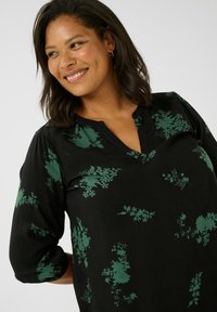 Schwarze Bluse mit grünen Blumenmustern, 3/4-Ärmel und V-Ausschnitt. Weicher Stoff mit lässiger Passform, geeignet für Freizeitkleidung.