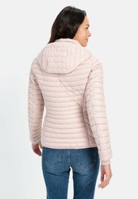Lyserød polstret jakke med hætte, med horisontal quilted design og en tætsiddende silhuet, båret over blå jeans.