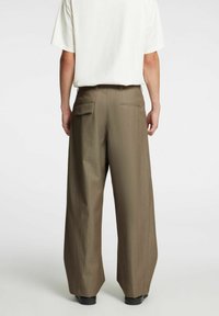 Brązowe spodnie o szerokich nogawkach wykonane z teksturowanej tkaniny, wyposażone w dwie tylne kieszenie z kontrastowym przeszyciem i luźnym krojem.