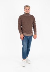 Bruine coltrui van textuurstof, gecombineerd met lichtblauwe jeans en witte sneakers. Over het algemeen casual kleding met een moderne fit.