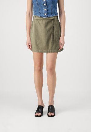 Green cotton wrap skirt with a tie belt, above-knee length, paired with a denim sleeveless top and black open-toed shoes.