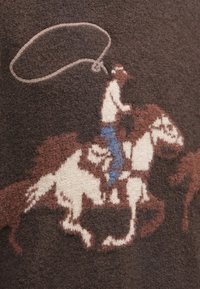 Πλεχτό πουλόβερ σε καφέ χρώμα με σχέδιο που απεικονίζει έναν καουμπόι σε άλογο, με λεπτομέρειες μπλε τζιν και λουρί. Μαλακή υφή.