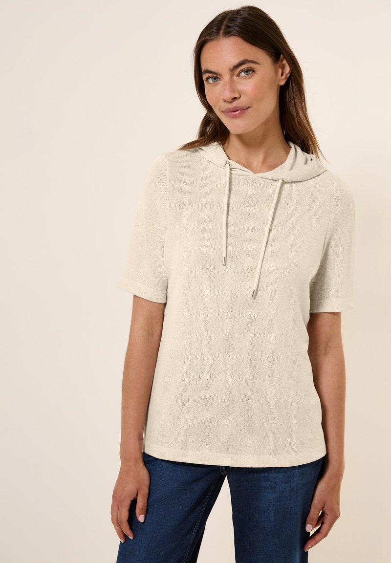 Felpa corta beige a maniche corte, realizzata in tessuto strutturato, con scollatura a coulisse e vestibilità comoda. Abbinata a jeans denim blu scuro.