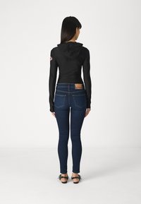 Μαύρο μπλουζάκι με μακριά μανίκια και κουκούλα, συνδυασμένο με μπλε στενά τζιν. Σημαντικές λεπτομέρειες περιλαμβάνουν μια καpatch απο το μανίκι και μια ετικέτα στα τζιν.