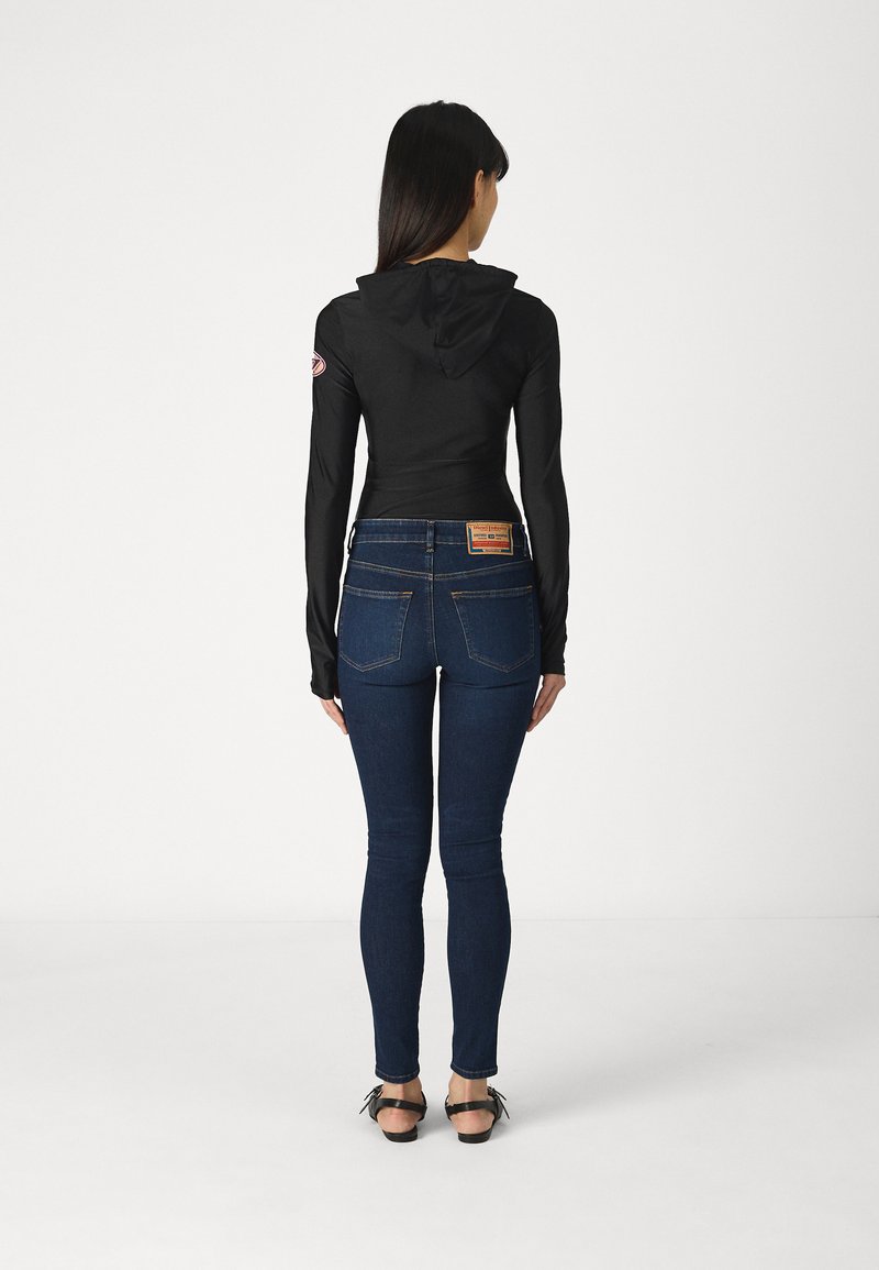 Czarny longsleeve z kapturem, w połączeniu z niebieskimi dżinsami skinny. Zauważalne detale to naszywka na rękawie oraz metka na dżinsach.